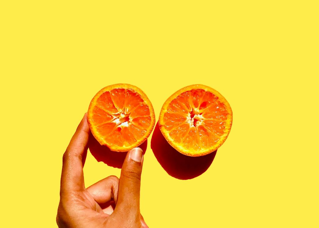 two halves of an orange being held in front of a yellow background